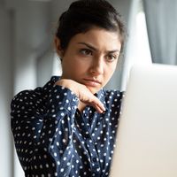 Businesswoman sitting at desk looking at laptop screen reading e-mail thinking, search issue solution feeling worried. 