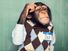 Young chimpanzee dressed in a shirt and sweater vest, scratching his head thinking. (primates)