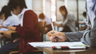 Close-up of hand of student holding a pen and taking an exam in a classroom (testing, tests, education).