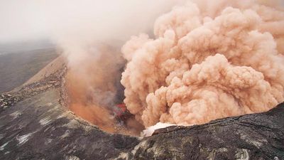 Ash cloud rising from the Kilauea Volcano Pu`u `O `o as crater floor collapses due to magma withdrawal. Incandescent rubble can be seen crumbling and rolling down the scarp. East rim of Pu`u `O `o is in the foreground, Kilauea, Hawaii on March 6, 2011.