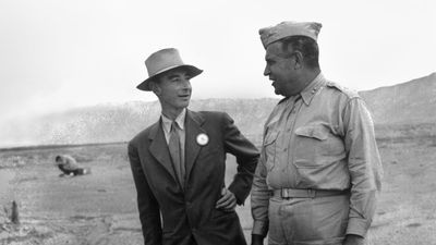 J. Robert Oppenheimer (L) & Gen. Leslie R. Groves at ground zero examine remains of a base of the steel test tower at the Trinity Test site of a nuclear bomb; as part of the Manhattan Project in New Mexico, Sep. 1945. Los Alamos National Laboratory