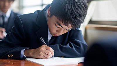 Japanese student boy doing schoolwork in a classroom at the school. Stock photo.