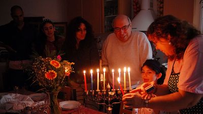 Judaism - Hanukkah. Jewish family lighting a candle on a menorah. Also called Festival of Lights or Feast of Lights.