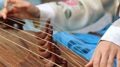 A woman wearing a hanbok plays the traditional Korean musical instrument kayagum (gayageum).