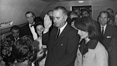 Jacqueline Kennedy and Lady Bird Johnson stand by President Lyndon B. Johnson as he takes the oath of office aboard Air Force One after the assassination of John F. Kennedy, November 22, 1963.