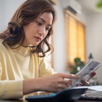 A woman looks at some papers and her computer.