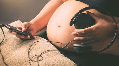 Pregnant woman holding headphones on her belly