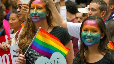 Young women with rainbow painted faces - symbol of lesbian, gay, bisexual and transgender - LGBT - watch the San Francisco Pride Parade in 2015. Gay pride human rights civil rights spectators California